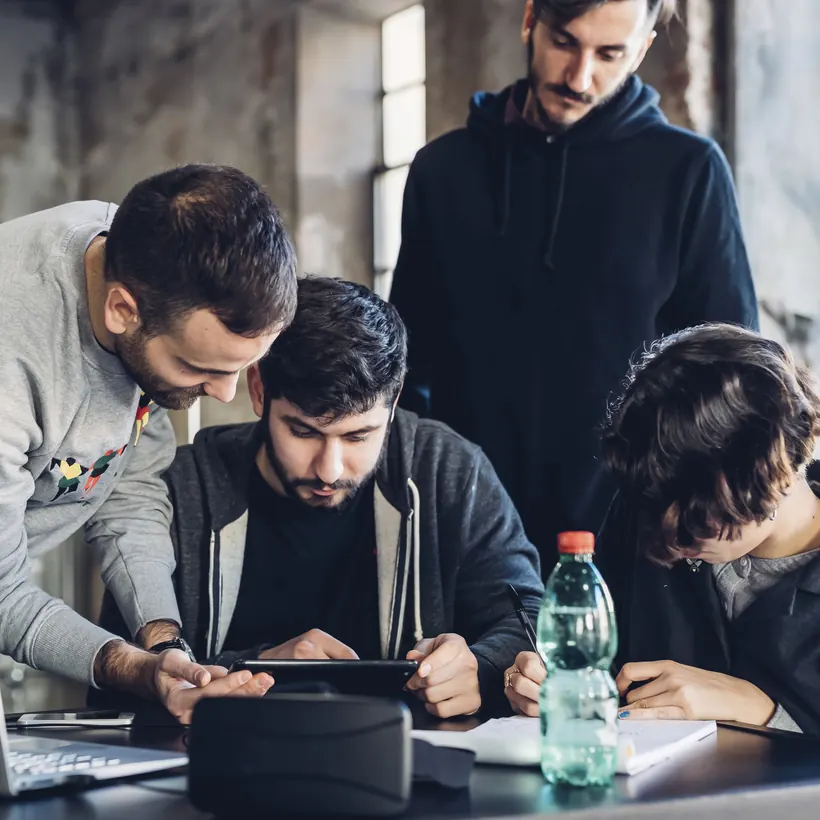 Sfida a squadre: quattro colleghi chini su un tablet attorno al tavolo
